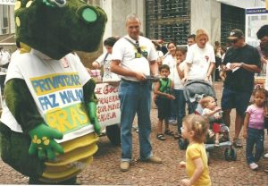 Atividade de rua durante a Feira do Livro de Porto Alegre, em 2001. De pé, ao lado do boneco “Sau, o dinossauro”, está o criador da marca, o então diretor do Sindipetro-RS, Gerson Luís Pereira Pires